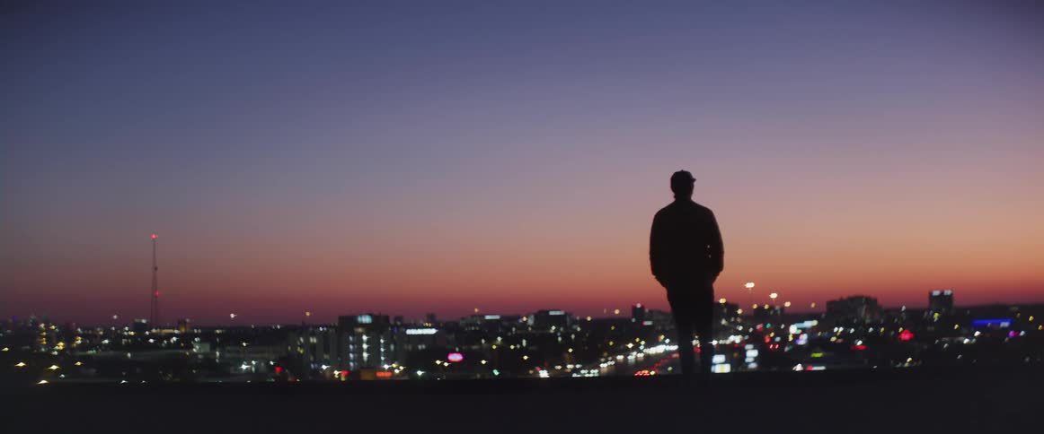 A man stands and looks towards a city skyline at dusk