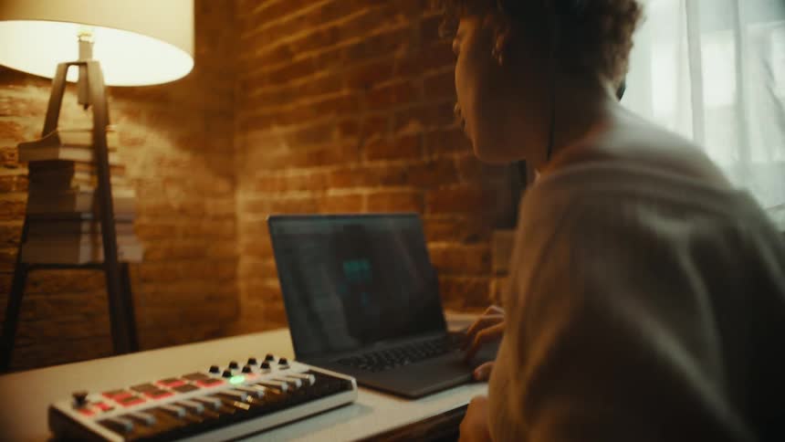 A woman sits at a table with a laptop and sound mixer
