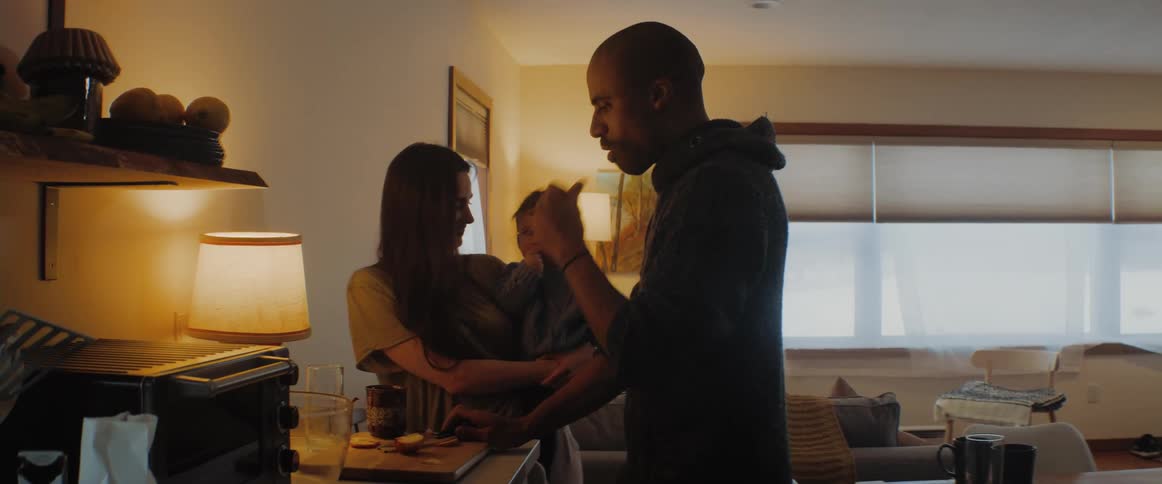 A man eats something while a woman holds a baby