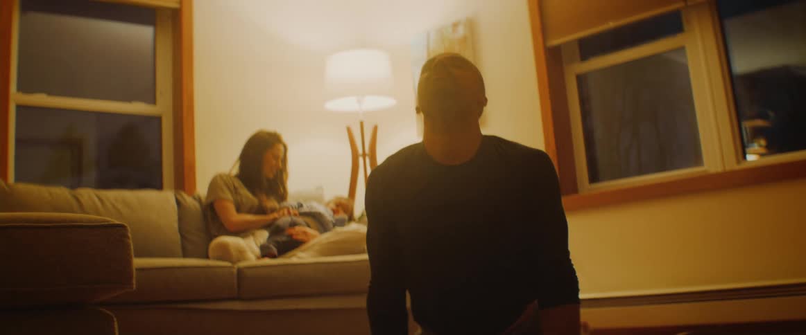 A man is doing yoga as his family sits on the couch