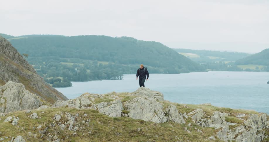 Man hiked across rocks and moss on shore near lake with mist covered forest in the background
