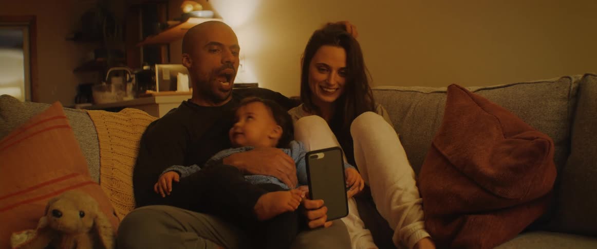 A man and woman sit with a baby having a video call on a cell phone
