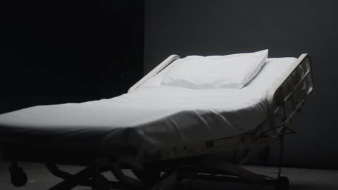 Hospital bed and a white pillow sit in an empty room
