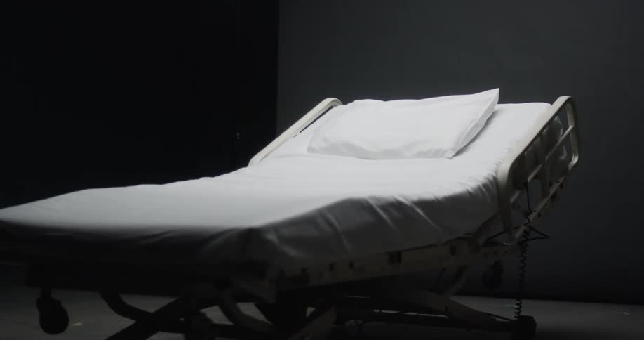Hospital bed and a white pillow sit in an empty room