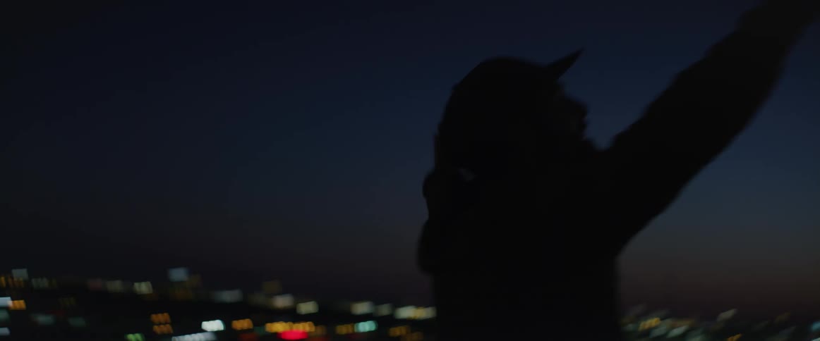 Man standing at the top of a building with a big city in the background spinning around with open arms during sunset