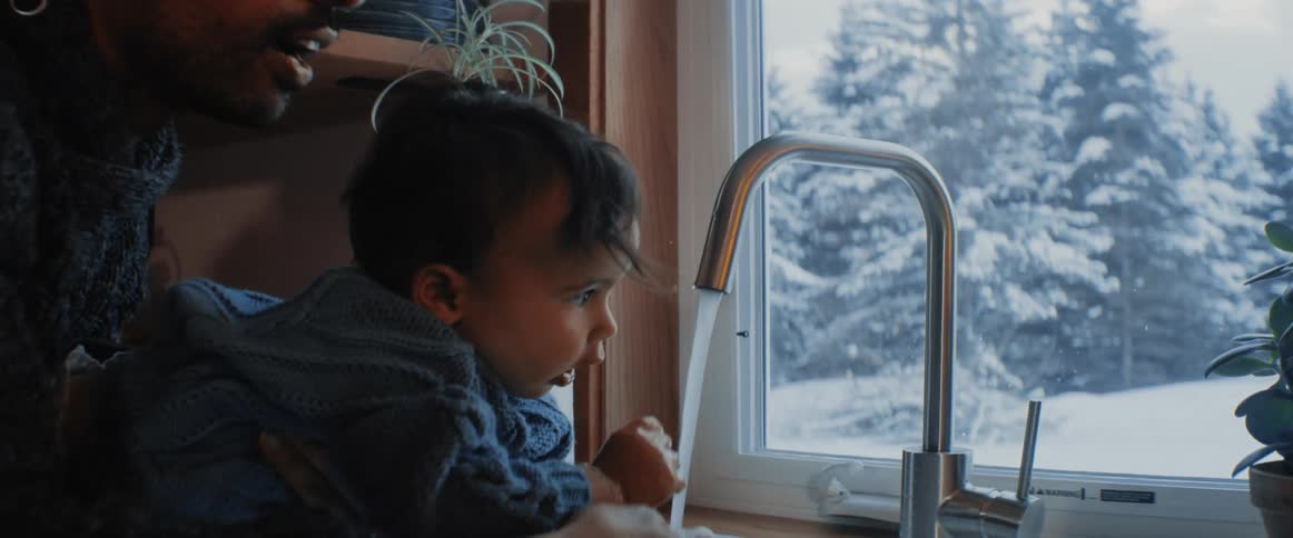 A man holds a small baby at a kitchen to wash their hands