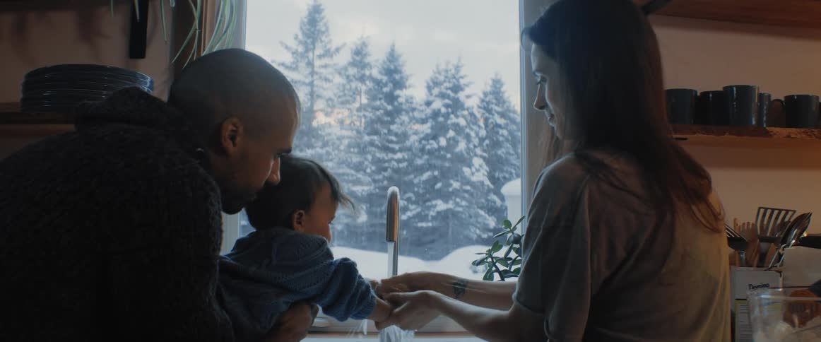 A man holds his son over the kitchen sink as his mother washes his hands