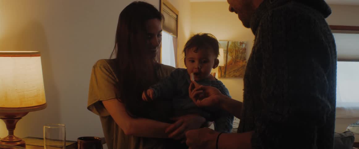 A woman holds a baby while a man feeds the baby a snack