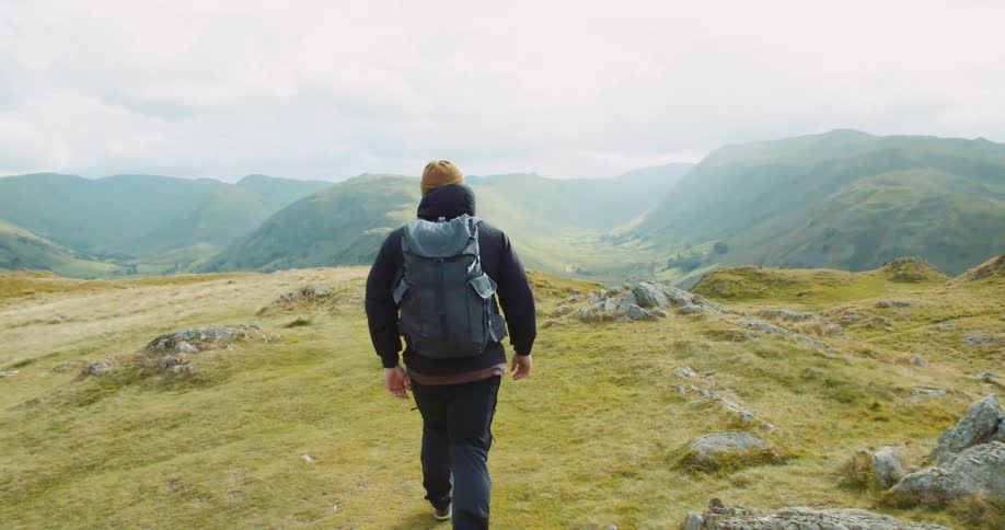 Man wearing a backpack and walking towards a cliff with a view of several hills ahead