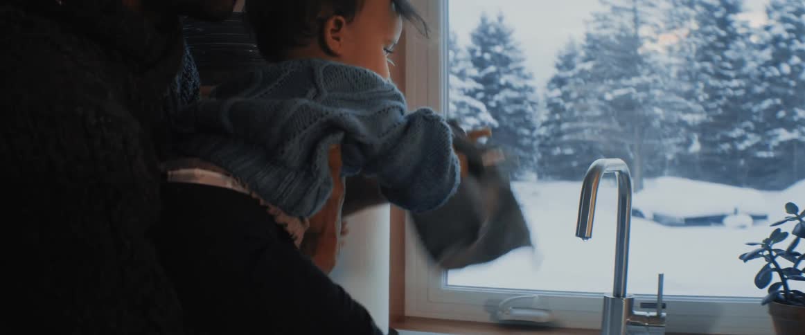 A man laughs as his son tries to play with water from the kitchen sink