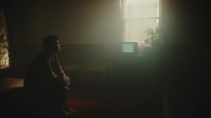Young man sits in a room and looks at an older television that is showing only static