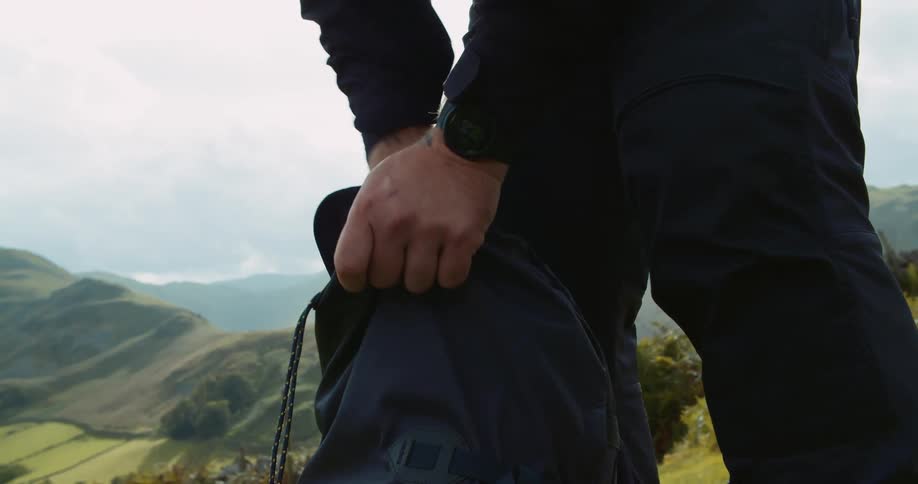 A man undoes the drawstring on a bag and unpacks his gear overlooking valley and ridge
