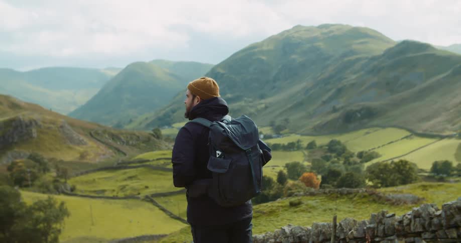A man stands outside and looks at the rolling hills in front of him