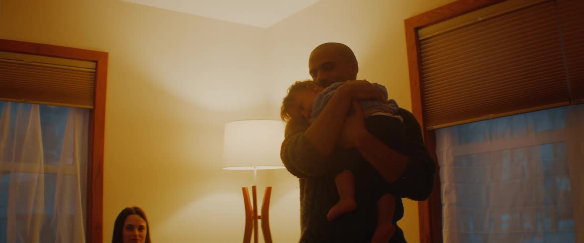 A man standing in the living room hugging and rocking his baby girl as mom looks on