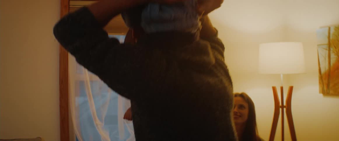 A man bounces a baby on his shoulder and jumps around a living room