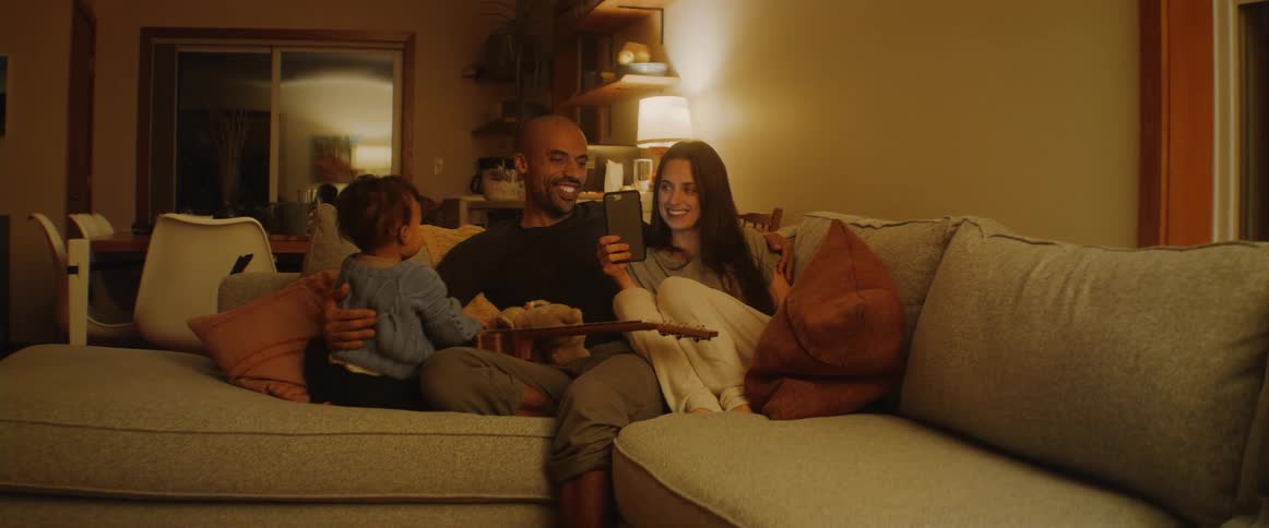 A family sits on the couch together and watches a smartphone