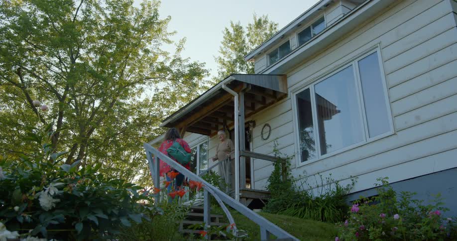 Elderly women walks onto porch to greet visiting family