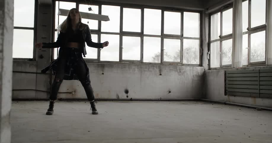 A blond woman dances inside an empty room during the day