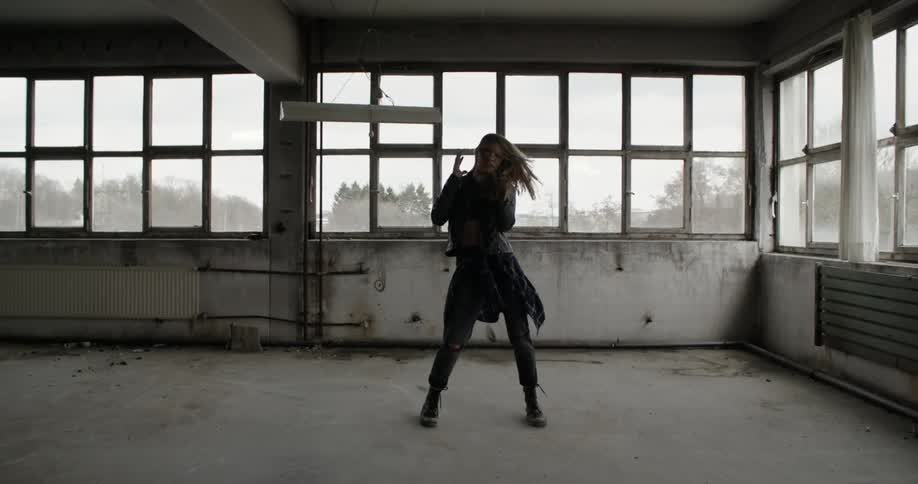 A woman in black dances in a windowed warehouse