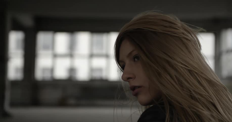 A woman looks over her shoulder in an abandoned building and throws her head around