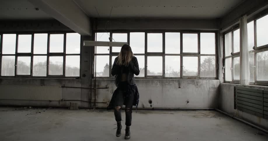 A woman in a leather jacket dances in an empty warehouse