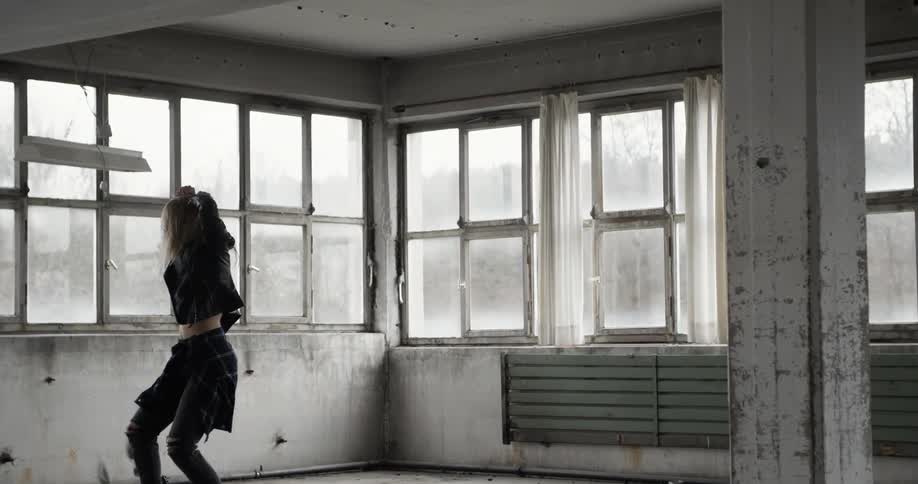 A woman in dark clothing dances in a windowed room