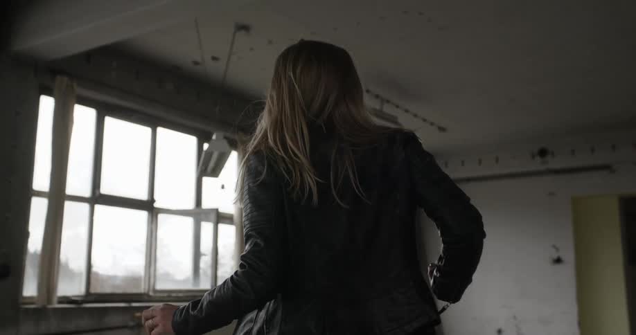 A woman in a leather jacket dances in a warehouse