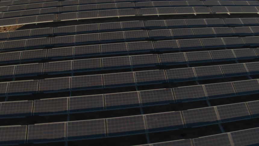 The sun is shining brightly on solar panels on a solar farm with trees and a mountain in the distance
