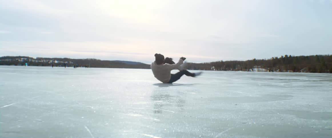 Woman figure skates on the frozen lake and falls while doing a spin