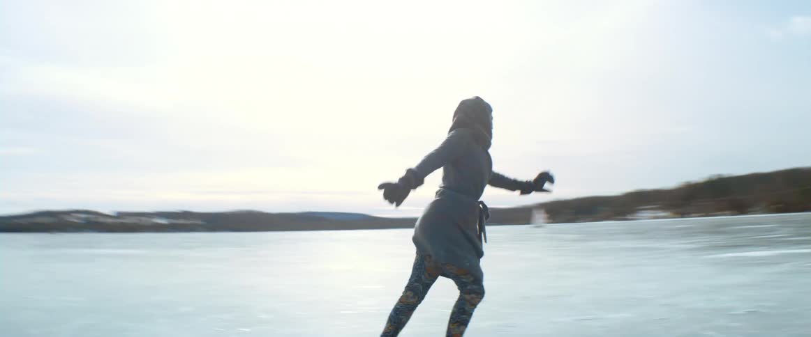 A woman skating on a frozen lake jumps and turns in the air