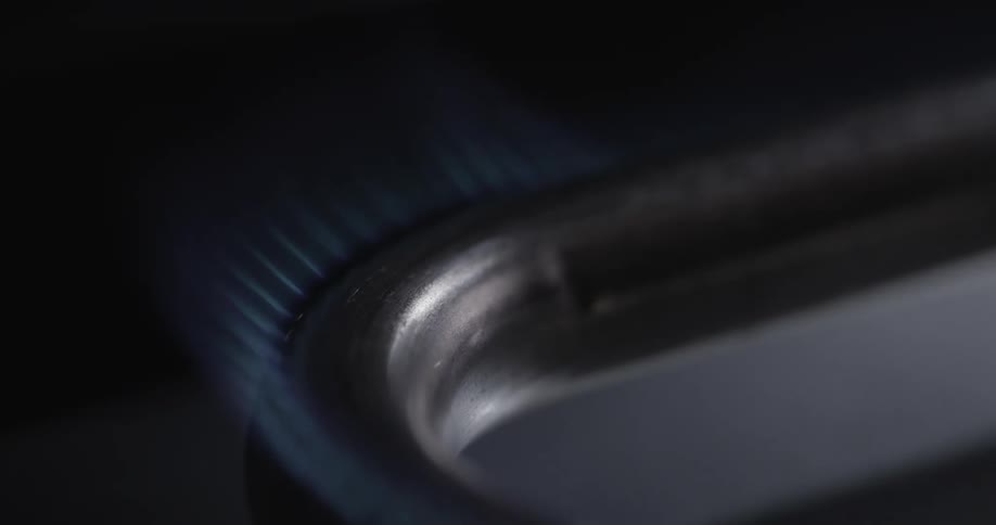 A flame ignites a burner on a gas stove and it is encircled with blue flames
