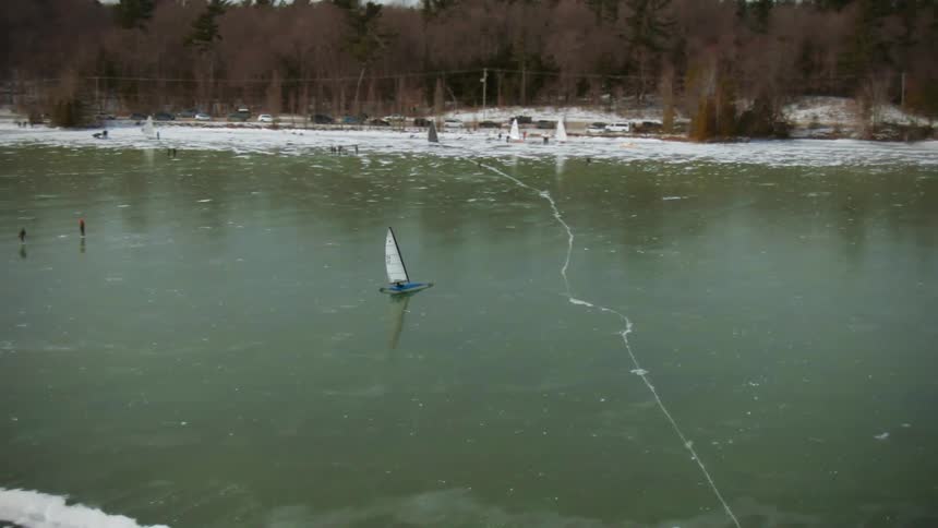 An aerial view of a frozen lake with people walking on it and ice sailing in a vessel in the daytime