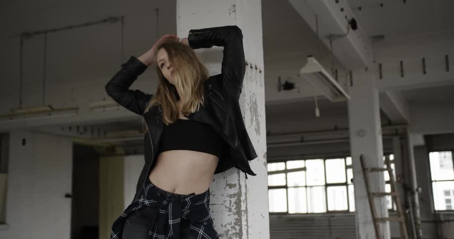 A woman in a black jacket dances against a chipped white pillar