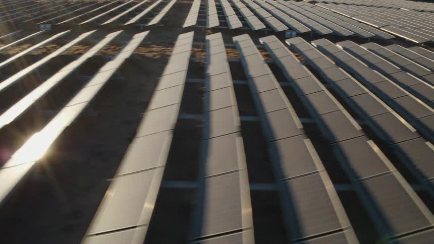 The sun is shining brightly on solar panels on a solar farm