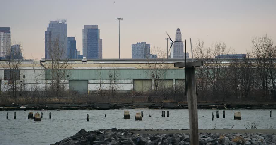 A lone windmill spins in an old part of a citys waterway along with the remains of an old pier in the evening
