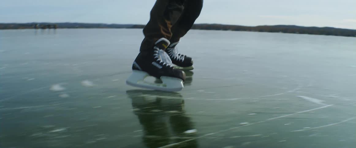 A man skates backwards on a frozen lake while his friend twirls on the ice