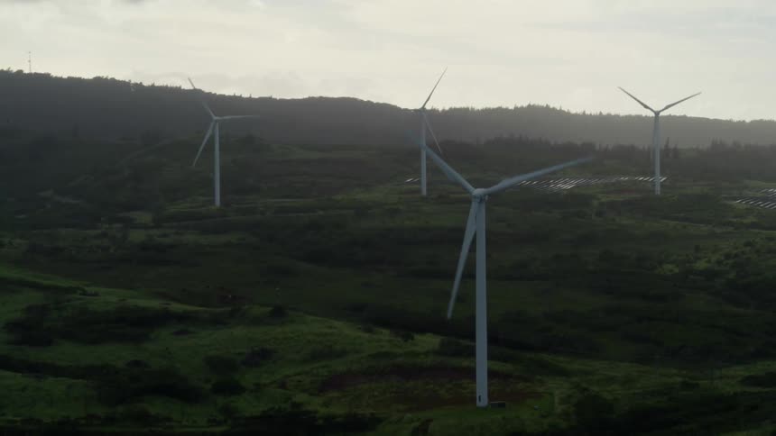 Wind turbines are turning on a hillside under a cloudy sky