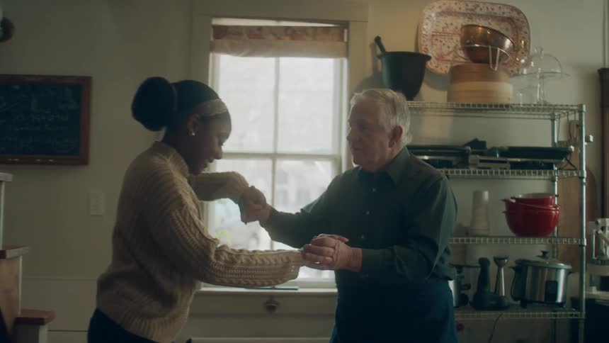 A man and woman laugh as they dance in their kitchen