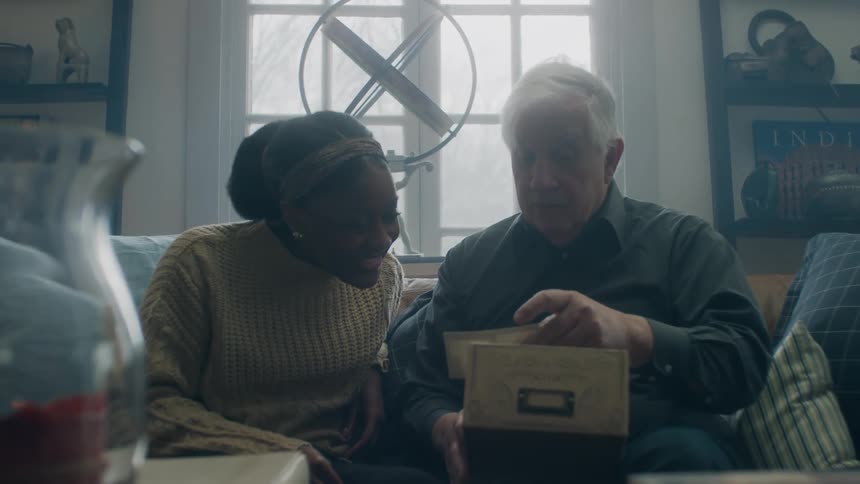 A man in his home is sitting on a sofa and sharing memories with a young woman