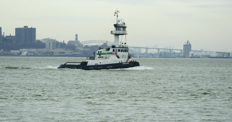 A tugboat travels through the water with a city bridge behind