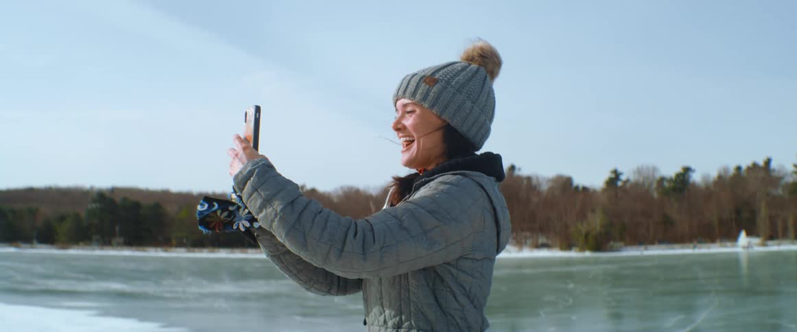 A woman is standing on a frozen lake taking a photo on a cold winter day