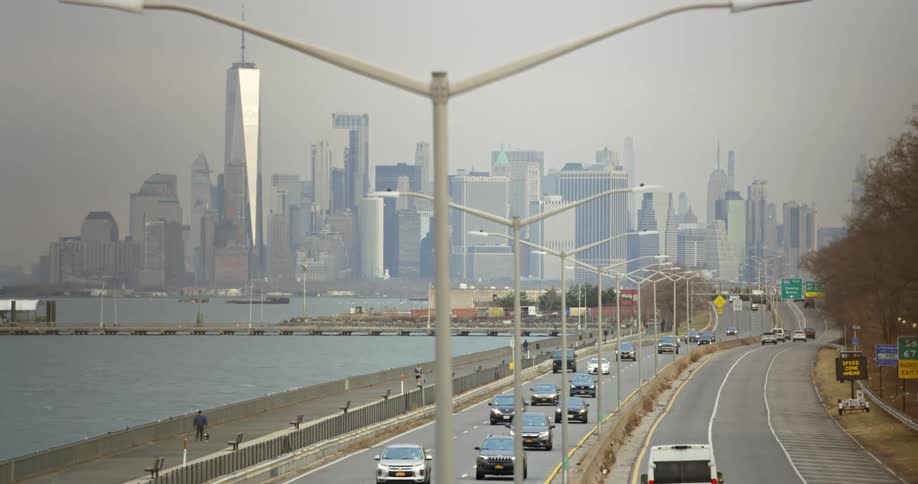 Traffic flows to and from fog covered city as man walks his dog on beach near highway