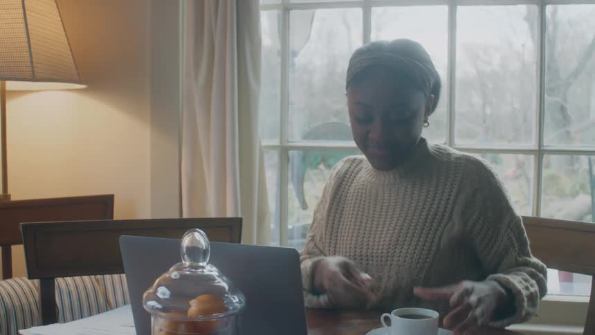 Old white man and black woman sitting in the table talking and drinking coffee while she is handling some papers and using a laptop