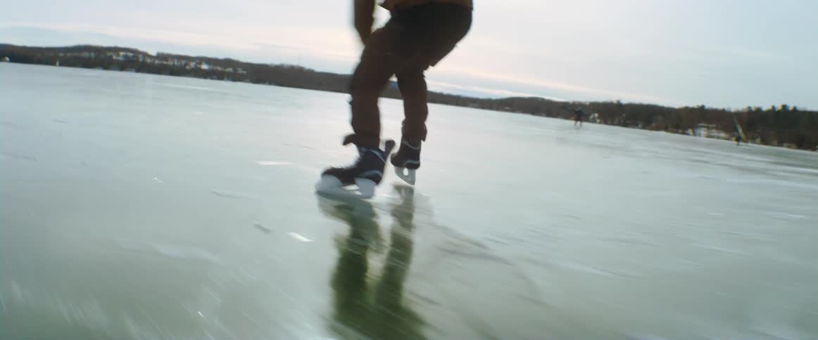 A male teenager wearing hockey skates skating off on a frozen lake
