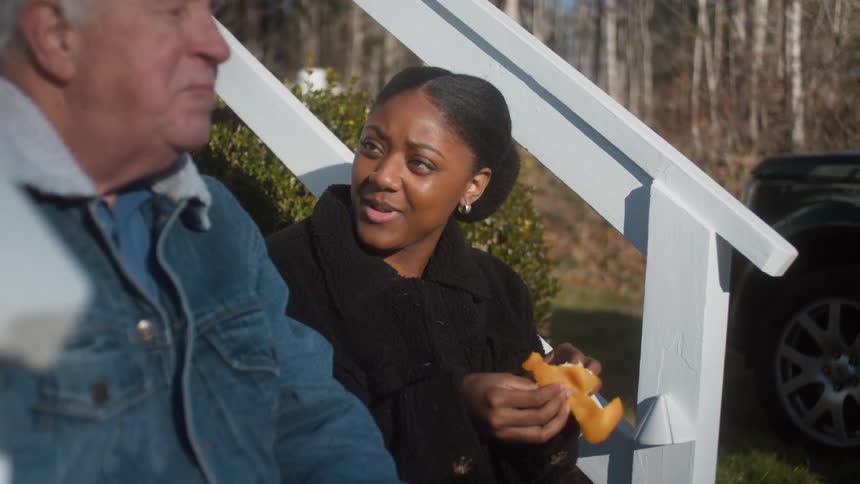 An elderly man sitting on steps talking with a young woman sharing an orange
