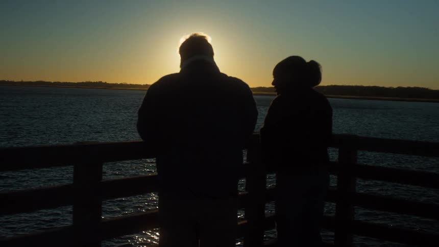 A man and woman watch the sunset by the water