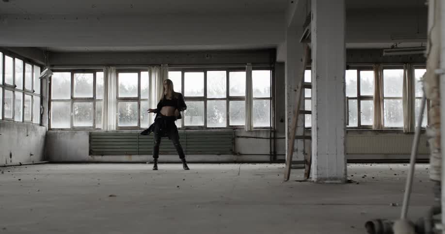 A woman in black dances around an empty warehouse