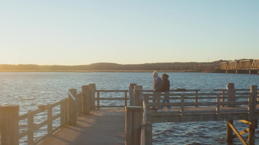 A man and woman walk along a lakeside pier together
