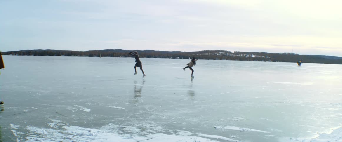 Two friends twirl and leap as they skate on the lake