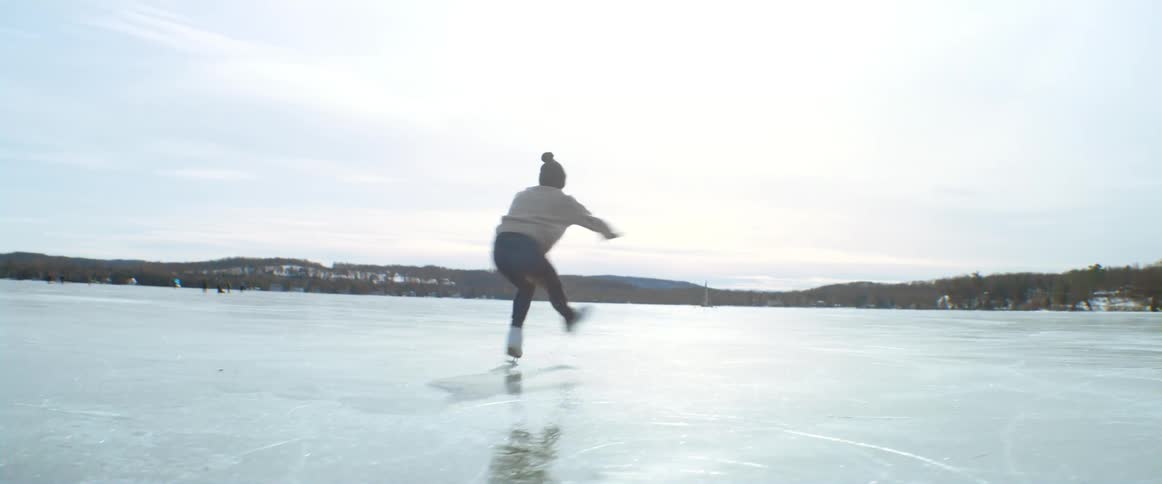 Female spinning on ice skates then falling on a frozen lake